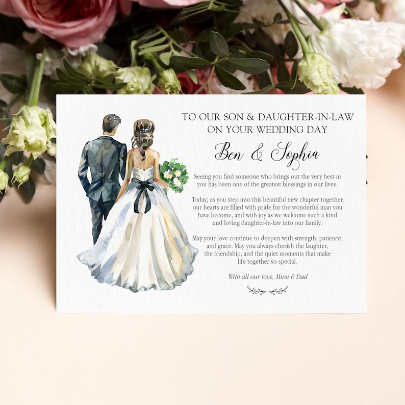 Puede incluir: Una tarjeta de boda rectangular con una ilustraci&oacute;n en acuarela de una pareja vista desde atr&aacute;s, el novio con traje oscuro y la novia con vestido blanco y faj&iacute;n negro. El texto dice: TO OUR SON & DAUGHTER-IN-LAW ON YOUR WEDDING DAY, Ben & Sophia, y un mensaje de amor de Mum & Dad.
