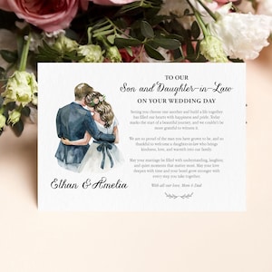 Puede incluir: Una tarjeta de boda rectangular con una ilustraci&oacute;n en acuarela de una pareja abraz&aacute;ndose. El texto dice: TO OUR Son and Daughter-in-Law ON YOUR WEDDING DAY, seguido de un mensaje, los nombres Ethan & Amelia, y With all our love, Mom & Dad.