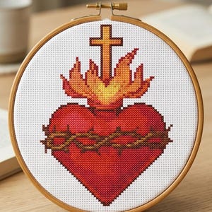 May include: A circular wooden embroidery hoop containing a cross-stitch pattern of a red Sacred Heart encircled by a brown crown of thorns, topped with a yellow and orange flame and a cross. The white fabric features the text MOCKUP IMAGE FOR DISPLAY PURPOSES ONLY.