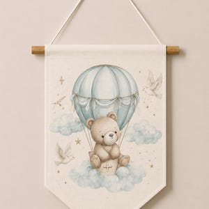May include: A cream-colored fabric wall hanging featuring a light blue hot air balloon carrying a brown teddy bear. The illustration includes soft blue clouds, two white doves, and small gold stars. The text Code: 8 is printed at the bottom.