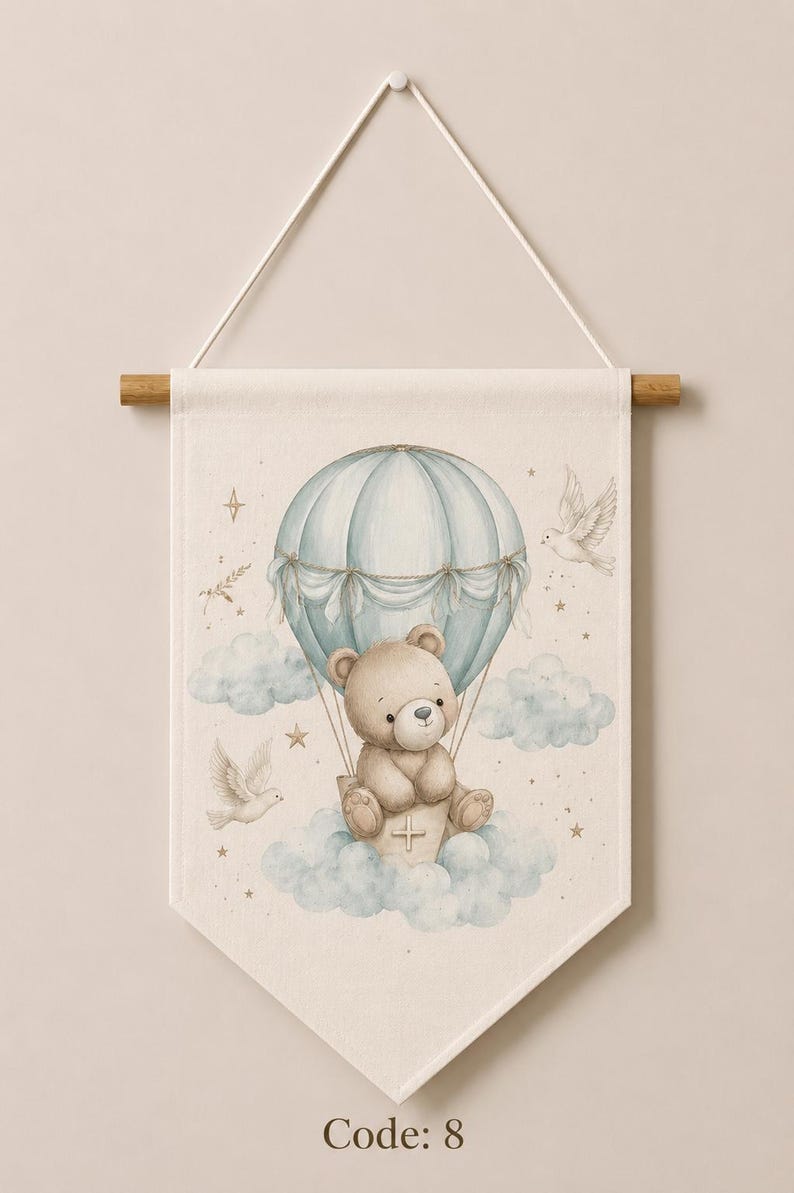 May include: A cream-colored fabric wall hanging featuring a light blue hot air balloon carrying a brown teddy bear. The illustration includes soft blue clouds, two white doves, and small gold stars. The text Code: 8 is printed at the bottom.