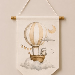 May include: A rectangular fabric wall hanging featuring a watercolor illustration of a beige and white striped hot air balloon with a wooden basket, a grey owl, a crescent moon, and grey clouds. The text Code: 10 is printed at the bottom.