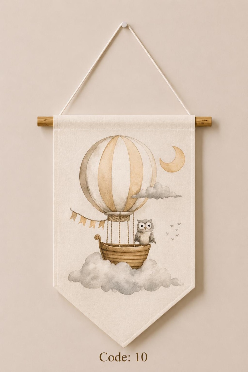 May include: A rectangular fabric wall hanging featuring a watercolor illustration of a beige and white striped hot air balloon with a wooden basket, a grey owl, a crescent moon, and grey clouds. The text Code: 10 is printed at the bottom.