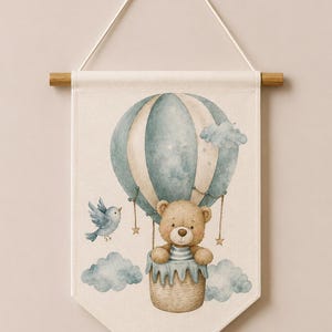 May include: A cream-colored fabric wall banner featuring a watercolor illustration of a brown teddy bear in a blue and white striped hot air balloon. A small blue bird flies nearby, surrounded by light blue clouds and the text Code: 9 at the bottom.