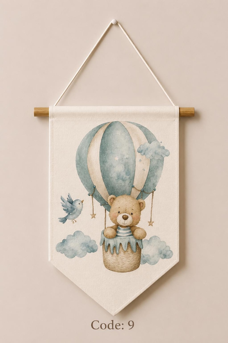 May include: A cream-colored fabric wall banner featuring a watercolor illustration of a brown teddy bear in a blue and white striped hot air balloon. A small blue bird flies nearby, surrounded by light blue clouds and the text Code: 9 at the bottom.