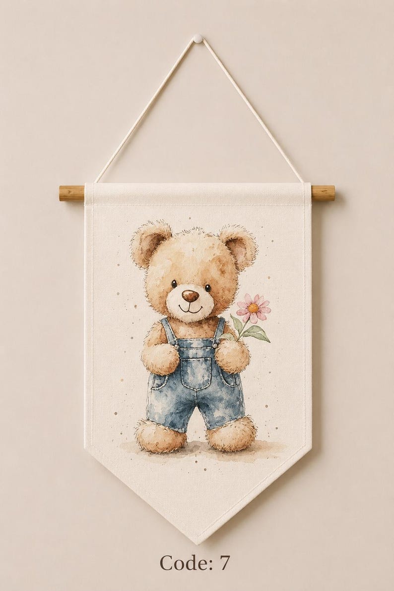 May include: A cream-colored fabric wall banner featuring a watercolor illustration of a light brown teddy bear wearing blue denim overalls and holding a single pink flower. The banner hangs from a wooden rod with a white string. The text Code: 7 is visible.