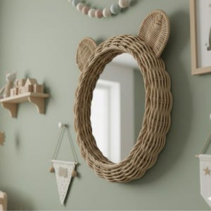 May include: A wall-mounted oval mirror featuring a woven light brown rattan frame with two prominent, rounded ears at the top. The mirror has a smooth, reflective glass surface and a natural, textured finish, creating a distinct animal-like shape.