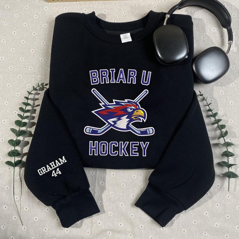 May include: Black sweatshirt with the text "BRIAR U HOCKEY" and a logo of a bird with crossed hockey sticks. The sleeve has the name "GRAHAM" and the number "44" printed on it. A pair of black headphones is in the background.