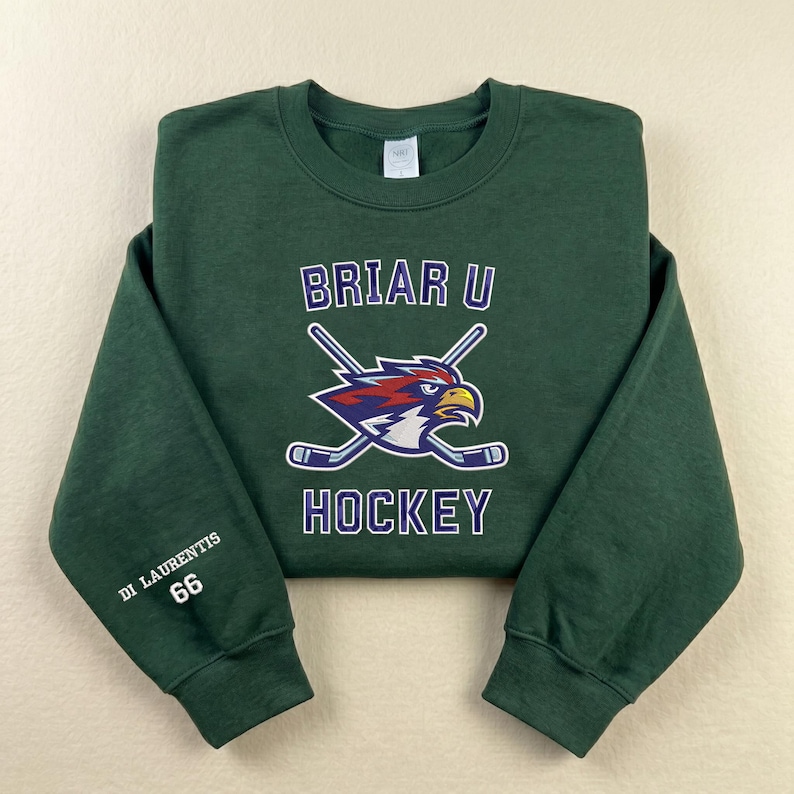 May include: A dark green sweatshirt with the text "BRIAR U HOCKEY" and a logo of a stylized eagle with crossed hockey sticks. The sleeve has the text "DI LAURENTIS 66".
