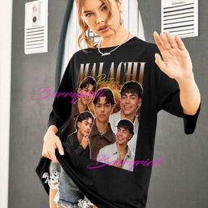 May include: Black oversized t-shirt with a gold gradient text reading "MALACHI Barton" and a collage of images. The shirt has a crew neck and three-quarter sleeves. The shirt is worn by a person.