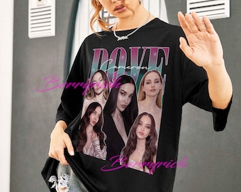 May include: Black t-shirt featuring a graphic of Dove Cameron with her name in a gradient font. The shirt displays multiple images of the actress. The shirt is worn by a person with denim shorts.