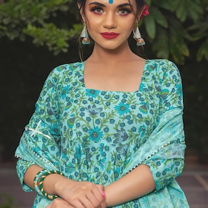 May include: A light blue square-neck kurta featuring a dark blue and green floral block print pattern, paired with a matching dupatta that has a silver scalloped trim along the edges, and green and gold bangles worn on the wrist.