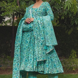 May include: A turquoise floral print long-sleeved dress with a matching dupatta and cropped trousers. The dress features a square neckline, a flared skirt with metallic trim, and a coordinating sheer scarf with decorative tassels and gold borders.