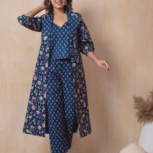 Könnte beinhalten: Ein dreiteiliges Outfit bestehend aus einem ärmellosen Oberteil mit V-Ausschnitt, einer weiten Hose und einem langen, vorne offenen Mantel. Das gesamte Set hat eine dunkelblaue Grundfarbe mit einem floralen Muster in Rosa, Grün und Weiß.