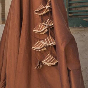 May include: A draped, brown fabric with decorative hanging tassels. The tassels are triangular, with a striped pattern in gold and brown, and trimmed with a white, scalloped edge. The fabric appears to be a heavy material.