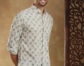 May include: A button-down shirt with a paisley pattern in shades of gray, pink, and white. The shirt is paired with blue jeans. The model is smiling and standing in front of a brown background.