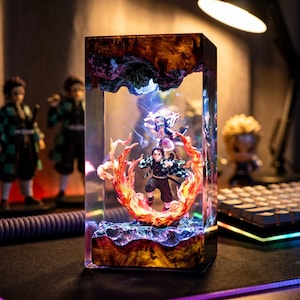 Op de afbeelding: Een rechthoekige harslamp met anime-figuren, vlammen en energie-effecten. De lamp heeft een houten look boven- en onderkant, met de figuren verlicht van binnen. Het kleurenschema omvat rood, oranje, blauw en bruin.