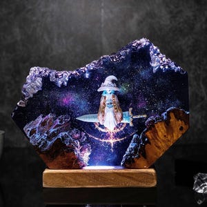 Pode incluir: Escultura decorativa em resina com uma figura de mago com uma espada, contra um fundo de gal&aacute;xia estrelada. A escultura &eacute; montada numa base de madeira, com ilumina&ccedil;&atilde;o interna que ilumina a cena da gal&aacute;xia. O mago usa um chap&eacute;u e uma capa.