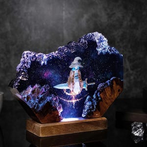 Pode incluir: Escultura em resina com um mago montado numa espada numa cena noturna estrelada. A escultura tem uma base de madeira e &eacute; iluminada com luzes azuis e roxas, criando um efeito m&aacute;gico. O mago usa um chap&eacute;u e uma capa.