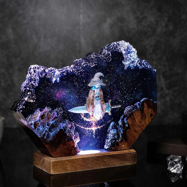 Pode incluir: Escultura em resina com um mago montado numa espada numa cena noturna estrelada. A escultura tem uma base de madeira e &eacute; iluminada com luzes azuis e roxas, criando um efeito m&aacute;gico. O mago usa um chap&eacute;u e uma capa.
