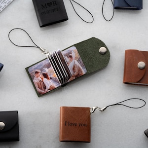 Op de afbeelding: Een verzameling kleine leren fotoalbums in verschillende kleuren, waaronder zwart, bruin en groen. Sommige albums zijn open en tonen afgedrukte foto's. E&eacute;n album is voorzien van de tekst "I love you".