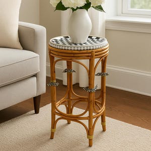 Op de afbeelding: Een bamboe bijzettafel met een zwart-wit geblokt blad, met een witte vaas gevuld met witte bloemen. Het frame van de tafel is van natuurlijk gekleurd bamboe. De tafel staat naast een beige bank.