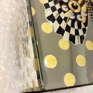 Pu&ograve; includere: Una scatola in vetro a specchio con una grafica decorativa a farfalla con motivi a scacchi bianchi e neri e accenti dorati. La superficie &egrave; decorata con un motivo ripetitivo di pois dorati, creando un aspetto riflettente e strutturato.