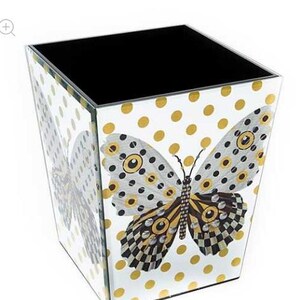 May include: A square wastebasket with a mirrored surface featuring a white background, gold polka dots, and a large butterfly graphic on the front. The butterfly has black, white, and gold wings with circular patterns. The interior is solid black.