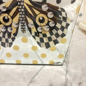 May include: A clear glass tissue box cover featuring a decorative butterfly graphic. The butterfly wings display a black and white checkered pattern with gold accents. The background of the glass is decorated with a pattern of gold and black polka dots.