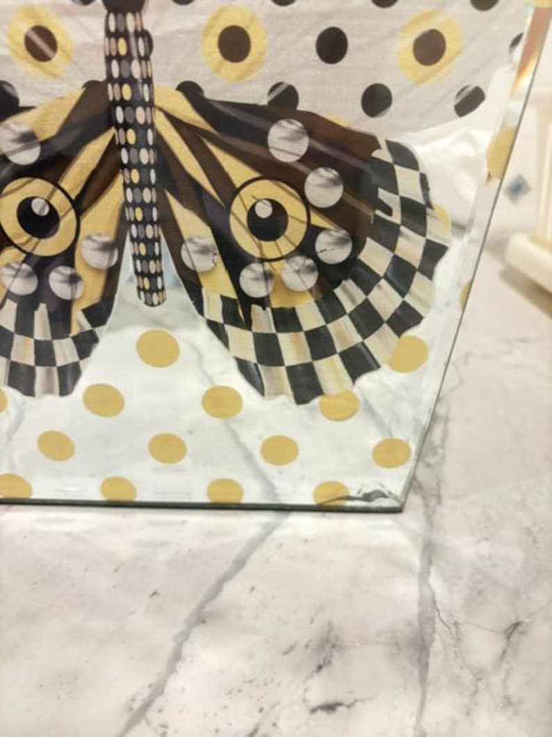 May include: A clear glass tissue box cover featuring a decorative butterfly graphic. The butterfly wings display a black and white checkered pattern with gold accents. The background of the glass is decorated with a pattern of gold and black polka dots.