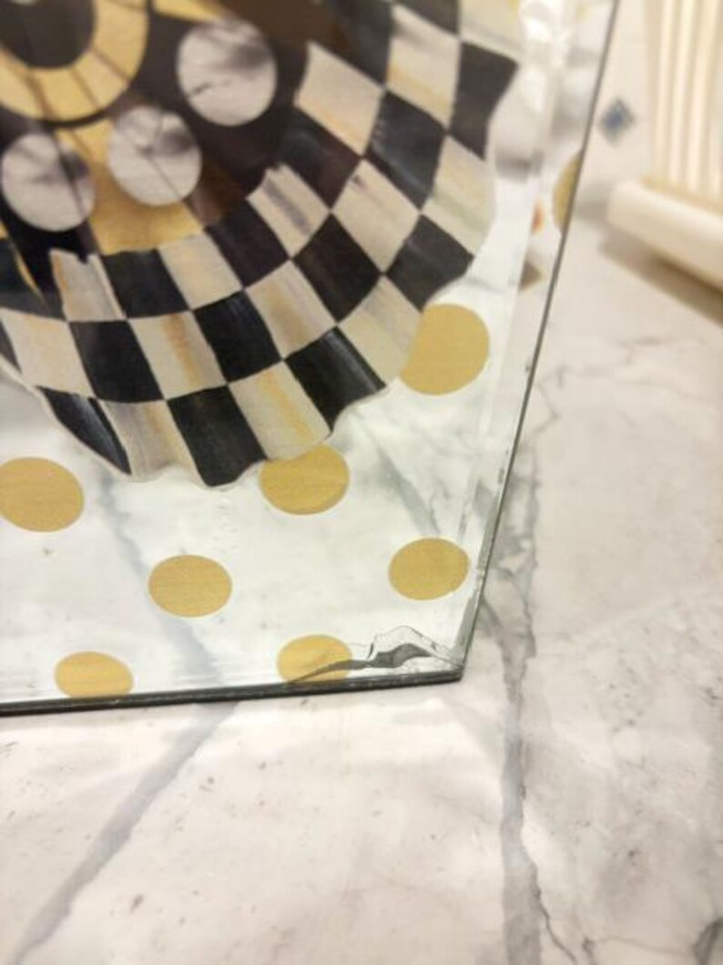 May include: A clear glass container featuring a decorative pattern of gold polka dots on the exterior and a black and white checkered design on the interior. The glass structure shows a visible crack near the bottom corner edge of the object.