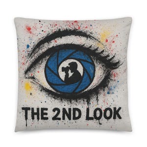Può includere: Cuscino quadrato con un design a occhio, un'apertura blu e la silhouette di un fotografo. Il testo "THE 2ND LOOK" è presente, con spruzzi di vernice colorati.