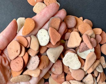 May include: A collection of small, smooth stones in shades of orange, tan, and cream. The stones vary in shape and size, with some appearing rounded and others more elongated. The image shows the stones held in a hand, showcasing their natural textures and colors.