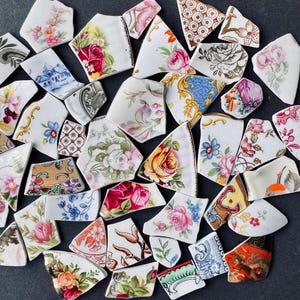 Op de afbeelding: Een verzameling gebroken porseleinen stukken met bloempatronen in verschillende kleuren, waaronder roze, geel, blauw en rood. De fragmenten zijn gerangschikt op een donkere ondergrond, waarbij de ingewikkelde ontwerpen van het originele serviesgoed worden getoond.