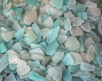 May include: A collection of sea glass pieces in various shapes and sizes. The colors range from pale blue and turquoise to clear and frosted white, with some pieces having a slight tan hue. The sea glass is smooth and tumbled, suggesting it has been shaped by the ocean.
