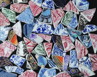 Op de afbeelding: Een verzameling gebroken keramische stukken met verschillende patronen en kleuren, waaronder blauwe bloemen, rood-witte wervelingen en zwart-witte ontwerpen. De fragmenten zijn gerangschikt op een zwarte ondergrond.