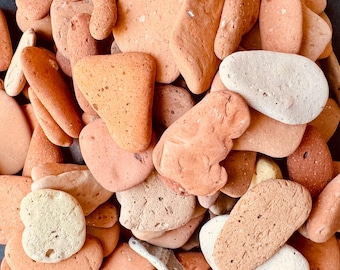 May include: A collection of smooth, rounded stones in shades of orange, peach, and cream. The stones vary in size and shape, with some being elongated and others more rounded. The texture appears to be smooth and natural, suggesting they are river rocks or similar.