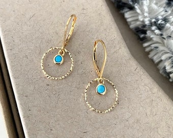 May include: A pair of gold earrings with a turquoise stone in the center of each circle.