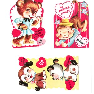 Può includere: Tre cartoline vintage di San Valentino con animali dei cartoni animati. La prima cartolina presenta un orso marrone con un vestito blu e che tiene un cuore rosso. La seconda cartolina presenta una scimmia con un cappello e che fa il pollice in su. La terza cartolina presenta due cani, uno marrone e uno bianco, con cuori rossi.