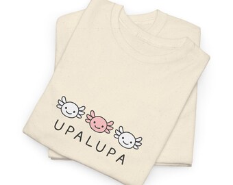 May include: Two cream-colored t-shirts are folded and stacked. The shirts feature a graphic of three smiling axolotls in white and pink, with the word "UPALUPA" printed below them in black.