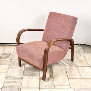 Op de afbeelding: Een vintage fauteuil met een stoffen zitting en rugleuning in oudroze. De stoel heeft gebogen, donkerhouten armleuningen en poten. Het ontwerp is eenvoudig en elegant, ideaal voor een woonkamer of leeshoek.