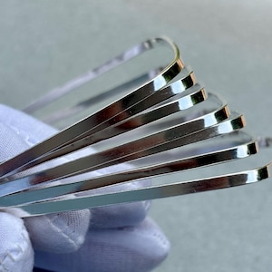 May include: A stack of shiny, silver-colored metal bangles. The bangles are thin, flat, and have rounded edges. The reflective surface of the bangles creates highlights and shadows. The bangles are stacked on top of each other.