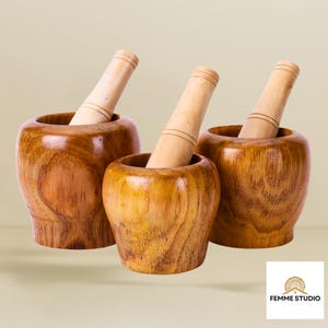 May include: Three wooden mortar and pestle sets. The mortars are a warm brown colour with visible wood grain. Each set includes a pestle, and the mortars vary slightly in size. The pestles are a light wood colour.
