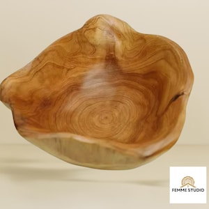 May include: A wooden bowl with an unusual, natural form. The bowl is crafted from light brown wood, displaying the wood's grain and texture. The bowl's uneven edges and smooth interior give it a rustic and elegant appearance.