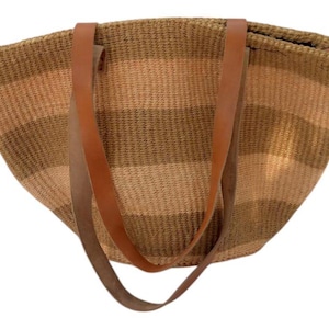Może przedstawiać: Tkana torba typu tote z brązowymi i beżowymi poziomymi paskami. Torba ma dwa brązowe skórzane uchwyty. Torba jest wykonana z naturalnego włókna i ma szeroki, otwarty top.