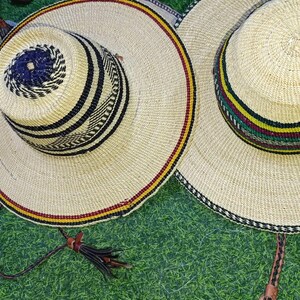 May include: Two woven straw hats with wide brims and decorative bands. One hat features a black and white pattern on the crown and a red and yellow band on the brim. The other hat has a striped band of green, yellow, and red. Both have leather tassels.