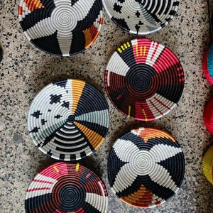 May include: A collection of six woven decorative bowls with intricate geometric patterns. The bowls feature a variety of colors, including black, white, orange, yellow, and red. The bowls are circular and appear to be handmade.