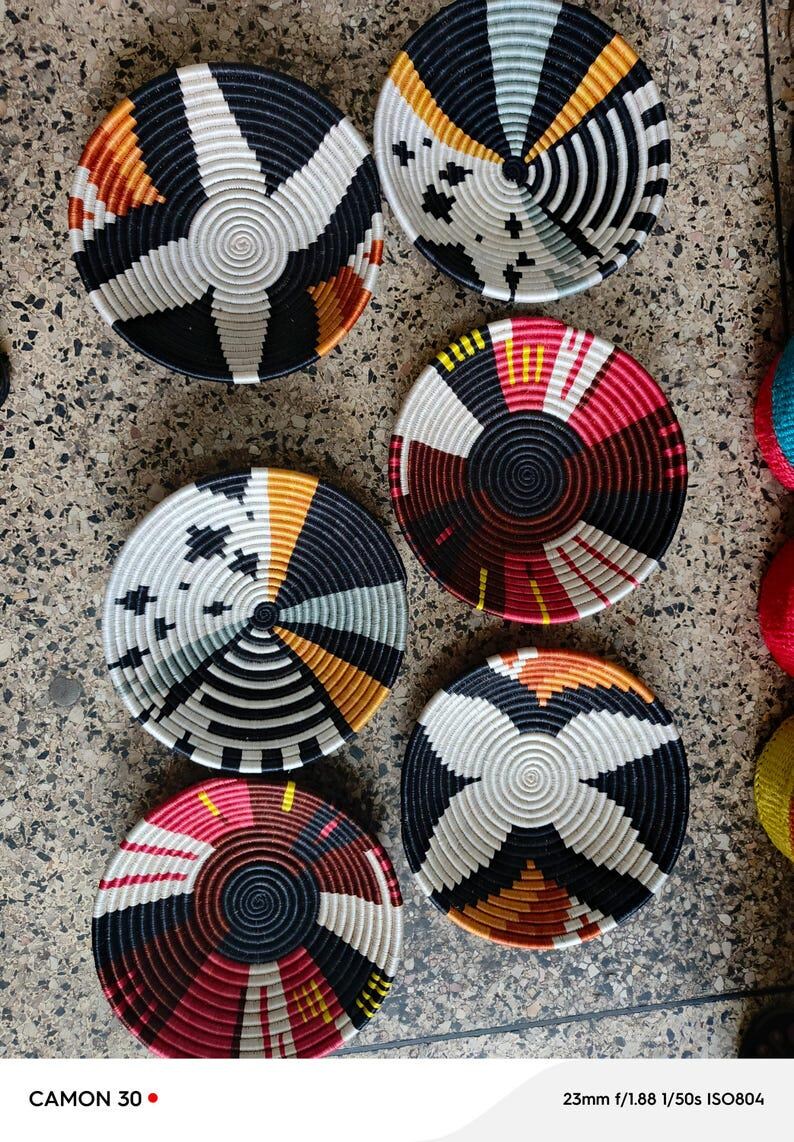 May include: A collection of six woven decorative bowls with intricate geometric patterns. The bowls feature a variety of colors, including black, white, orange, yellow, and red. The bowls are circular and appear to be handmade.
