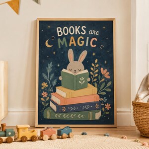 May include: A framed wall art print featuring a dark blue background with the text BOOKS are MAGIC. A light brown rabbit sits atop a stack of four colorful books, surrounded by stylized floral illustrations, a crescent moon, and stars.