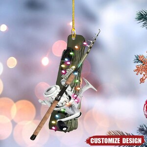 May include: A fishing-themed Christmas ornament. It features a fishing rod, reel, and a green case with the word "Hunter". The ornament is decorated with colourful lights and a gold string for hanging. The words "Customize Design" are at the bottom.